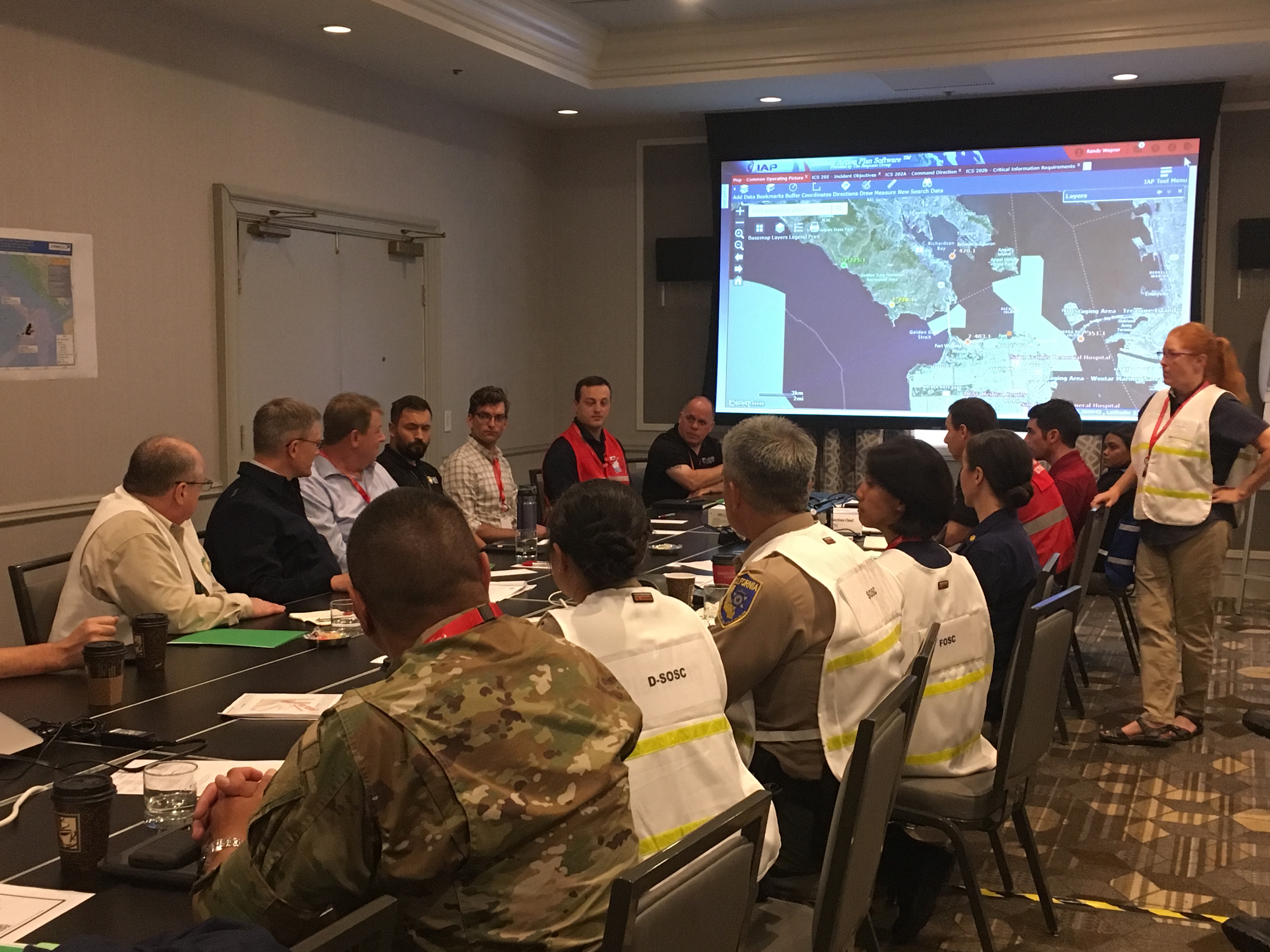 agency officials in vests sitting at table with large map on screen